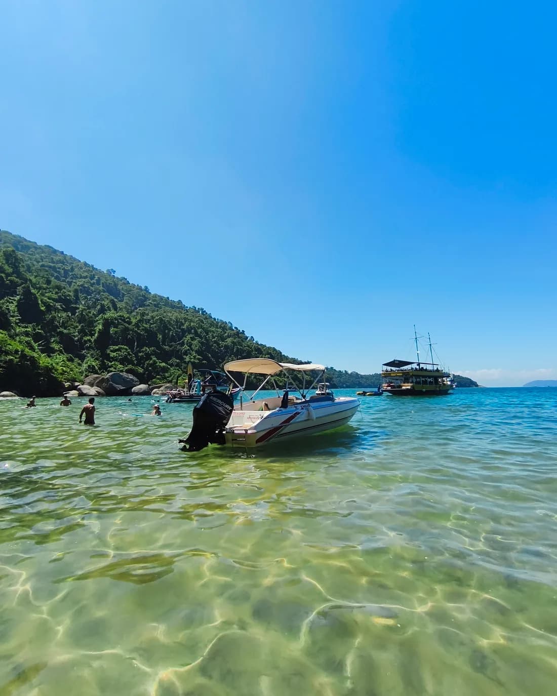 Lancha Oceania fundeada em água cristalina, com ilha coberta de mata ao fundo