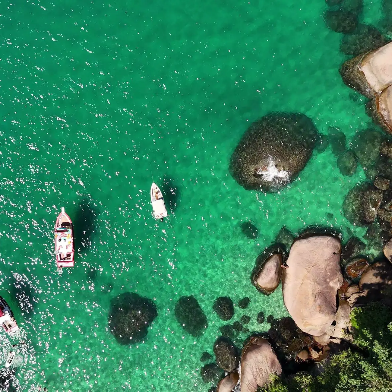 Vista aérea de barcos ancorados em água verde-esmeralda, entre afloramentos de pedra