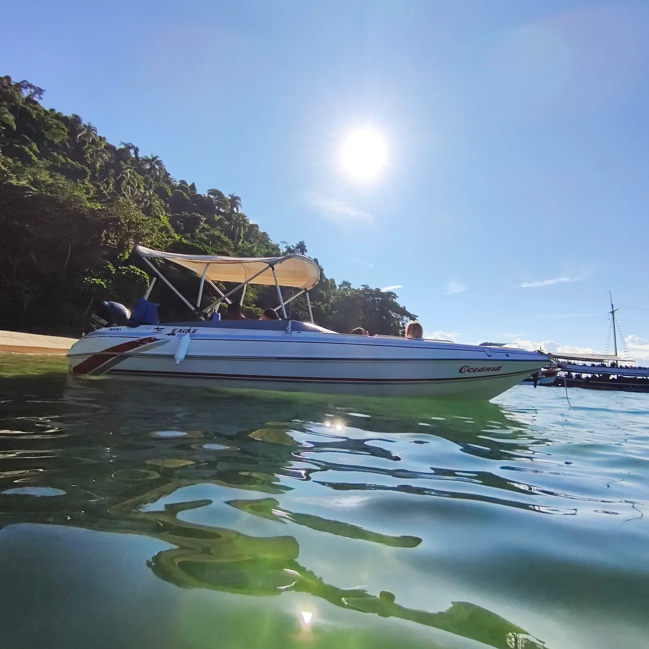 Lancha Oceania em contraluz, com o sol sobre a mata e reflexos na água