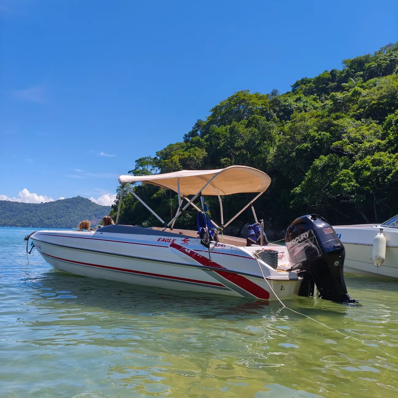 Lancha Oceania parada em frente a uma ilha, com montanhas ao fundo